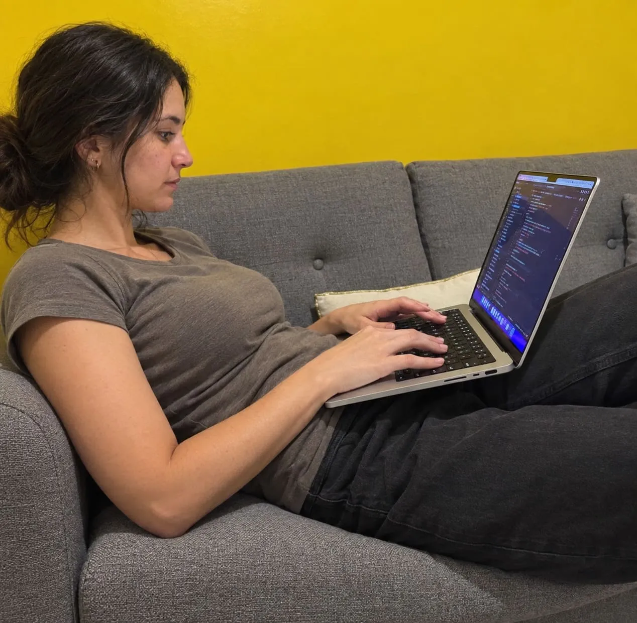 Someone sitting back on the office sofa, a laptop on their lap with a code editor open.